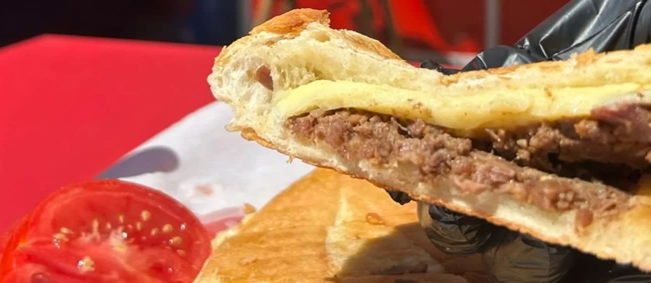 Dükkanda çekilmiş fotoğraf: eldivenli elde tost dilimi, arasında kavurma ve erimiş kaşar görünüyor.