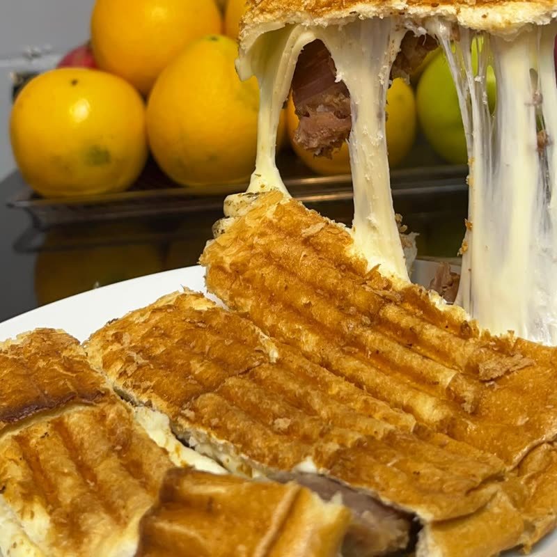 Dükkanda çekilmiş fotoğraf: eldivenli el tost dilimini kaldırıyor, kaşar uzuyor.